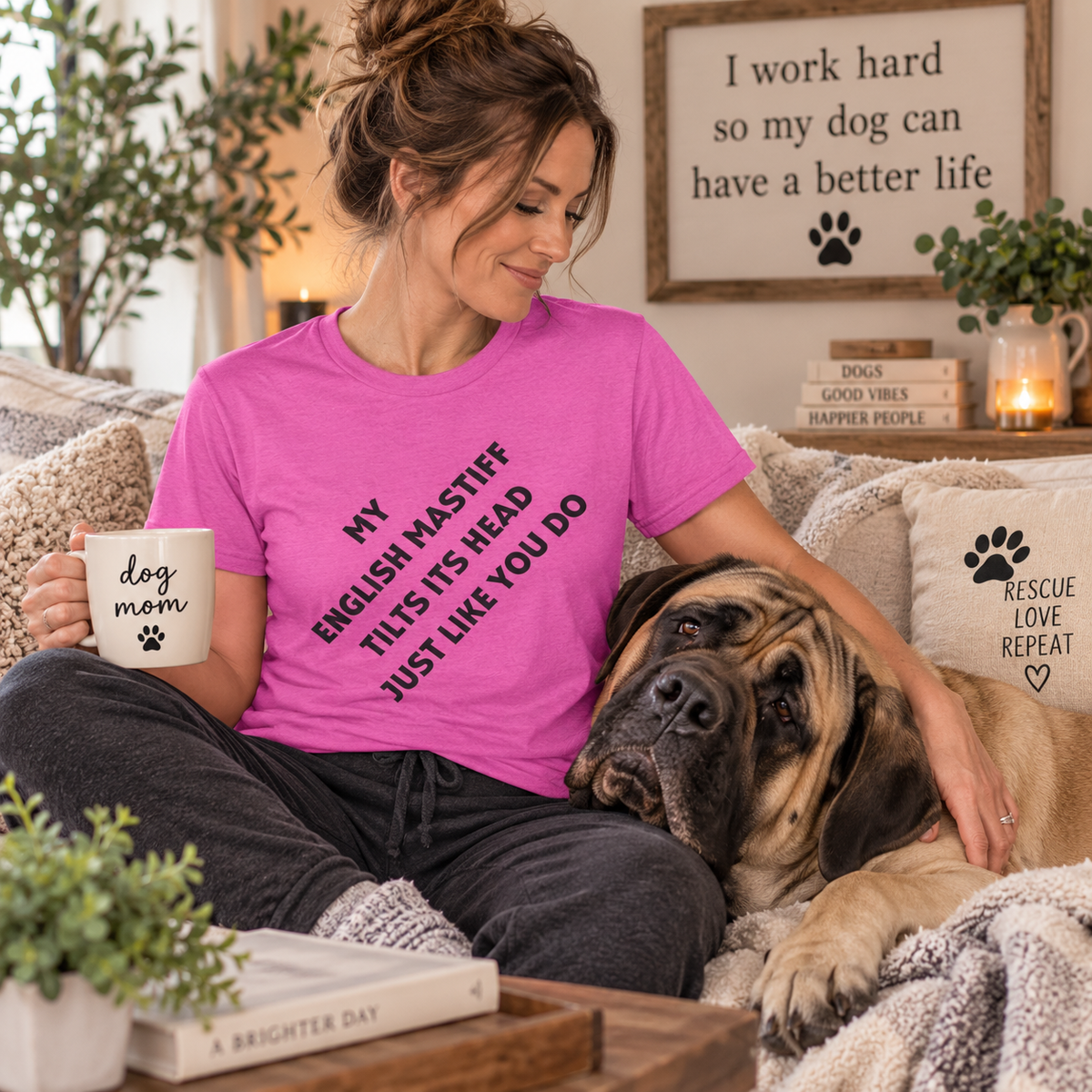  Woman wearing a pink English Mastiff head tilt t-shirt while sitting beside a large Mastiff on a cozy couch.