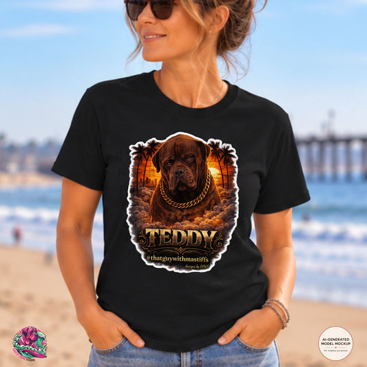 A woman wearing a black graphic t-shirt with a large print of a brown dog wearing a gold chain and the text 'TEDDY #thatguywithmastiffs' on the front, set against a beach background. Official That Guy With Mastiffs merch by Mastiff Mama Designs.